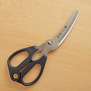 The award-winning Green Bell 'Takumi no Waza' kitchen shears, featuring curved stainless steel blades and black ergonomic handles, laid on a wooden surface.
