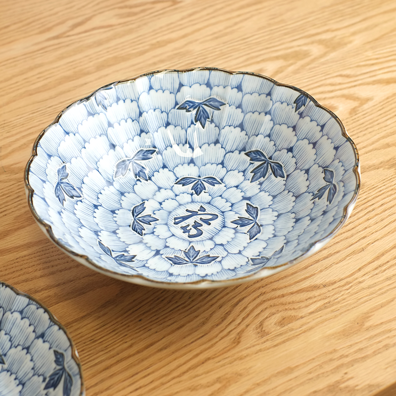 Hana Manyo blue and white Japanese serving bowl with dense chrysanthemum floral pattern and 福 fortune kanji at centre, with scalloped gold-rimmed edge, shown on a wooden surface