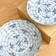 wo Hana Manyo blue and white porcelain serving pieces with dense chrysanthemum floral pattern and 福 fortune kanji at centre, shown with gold gift boxes on a wooden surface