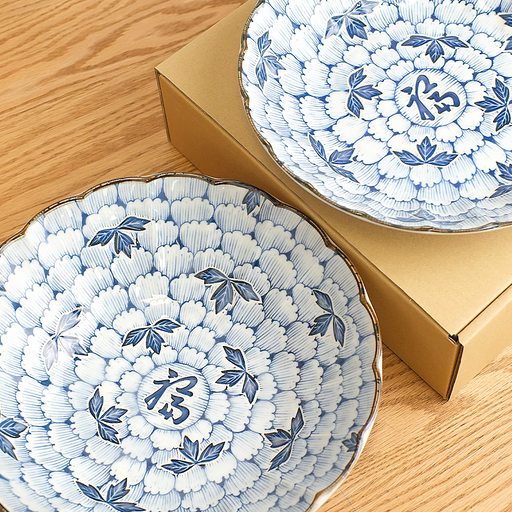 wo Hana Manyo blue and white porcelain serving pieces with dense chrysanthemum floral pattern and 福 fortune kanji at centre, shown with gold gift boxes on a wooden surface