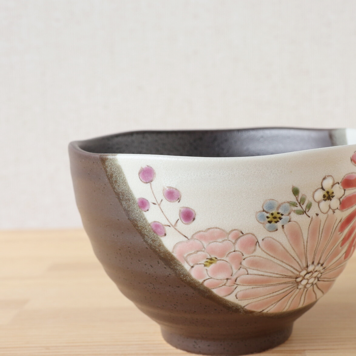 A side view of the Hana Floral Kutani bowl, highlighting the detailed hand-painted floral design. The bowl's speckled grey base is adorned with pink, red, and white flowers, along with small purple berries and blue blossoms. The gentle curve of the bowl and the textured surface are visible, emphasizing its handcrafted quality.