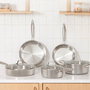 Happycall Stay 3-ply stainless steel cookware set of eight pieces including two frypans, a saute pan, saucepan, and pot with glass lids, displayed on a white kitchen bench.