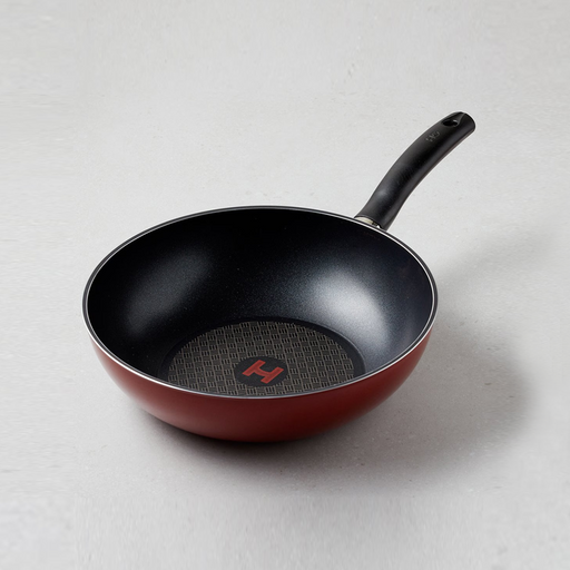 Happycall Diamond IH Solid Diamond Nonstick Induction Wok in matte black with stainless steel handle accent, displayed upright in its original packaging against a white kitchen background with stir-fried vegetables in the foreground
