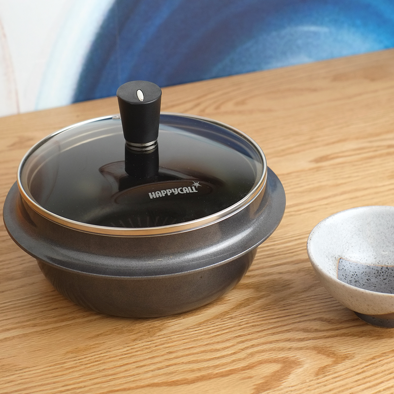 The black 18cm Happycall Korean Induction Cauldron (gamasot) with its wide, flat rim and matching glass lid, angled on a white background.
