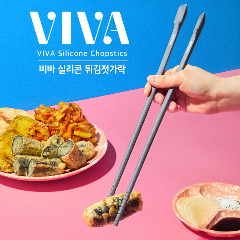 Hand using Happycall VIVA Silicone Chopsticks to lift tempura on a pink and blue background, showcasing their non-slip grip.

