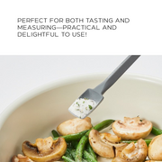 A small grey silicone spatula scooping seasoned salt from a bowl of sautéed mushrooms and green beans, illustrating practical use.


