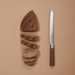 Happycall Woodique bread knife with wooden handle placed next to neatly sliced bread on a tan background.