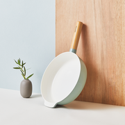 The 24cm Happycall Zium ceramic nonstick induction frypan, showing its sage green exterior, white cooking surface, light wood handle