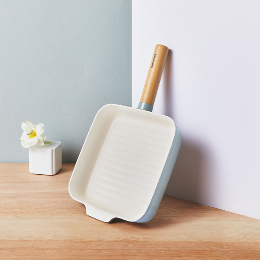 The square 22cm Happycall Zium ceramic nonstick induction grill pan, showing its sage green exterior, white ridged interior, and light wood handle, angled on a white background.