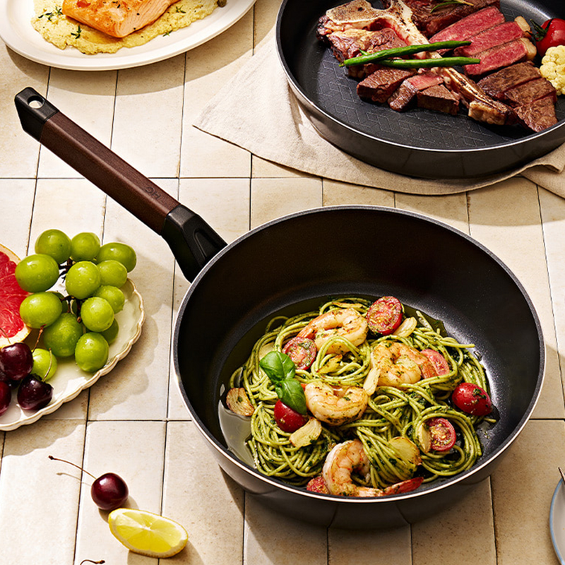 Happycall Royal wok filled with basil pesto pasta next to a steak dish.