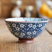 A lifestyle image of the Mino Yaki Hasui Cherry Blossom Japanese Bowl, showing its intricate blue and white floral pattern on a wooden table.