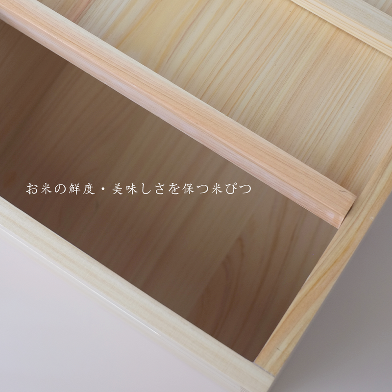 An overhead view of the Hinoki rice box filled with rice, showing the simple sliding lid mechanism and a traditional wooden masu measuring cup.

