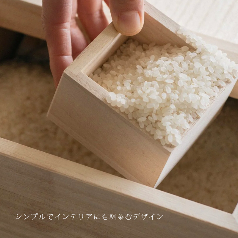 A hand scooping rice from the storage box with a traditional wooden masu cup, with Japanese text describing it as a simple design that blends with any interior.

