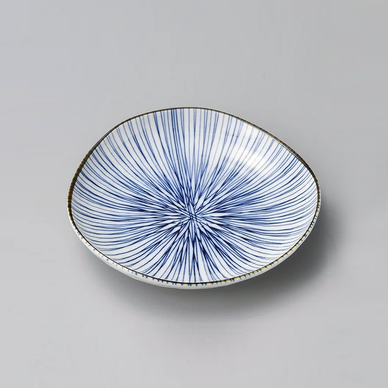A studio photo of the Ichiku Mino Yaki Fine Ten Grass Side Plate, showcasing its irregular shape and hand-painted blue lines radiating from the centre.