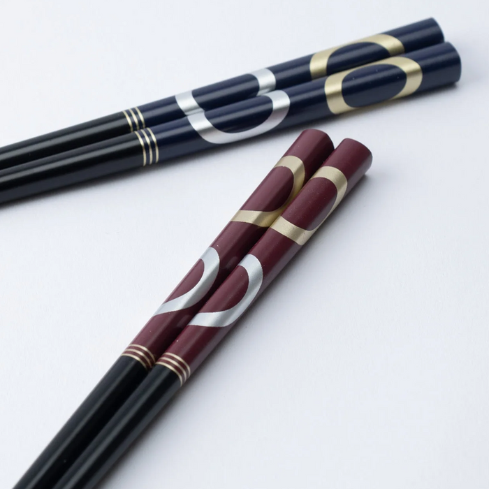 Close-up of Ishida Wakasa Nuri lacquered chopsticks featuring gold and silver overlapping ring patterns on burgundy and navy handles.