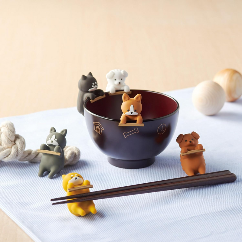 A collection of cute, dog-shaped Japanese chopstick rests (hashioki) in various styles, arranged around a soup bowl.