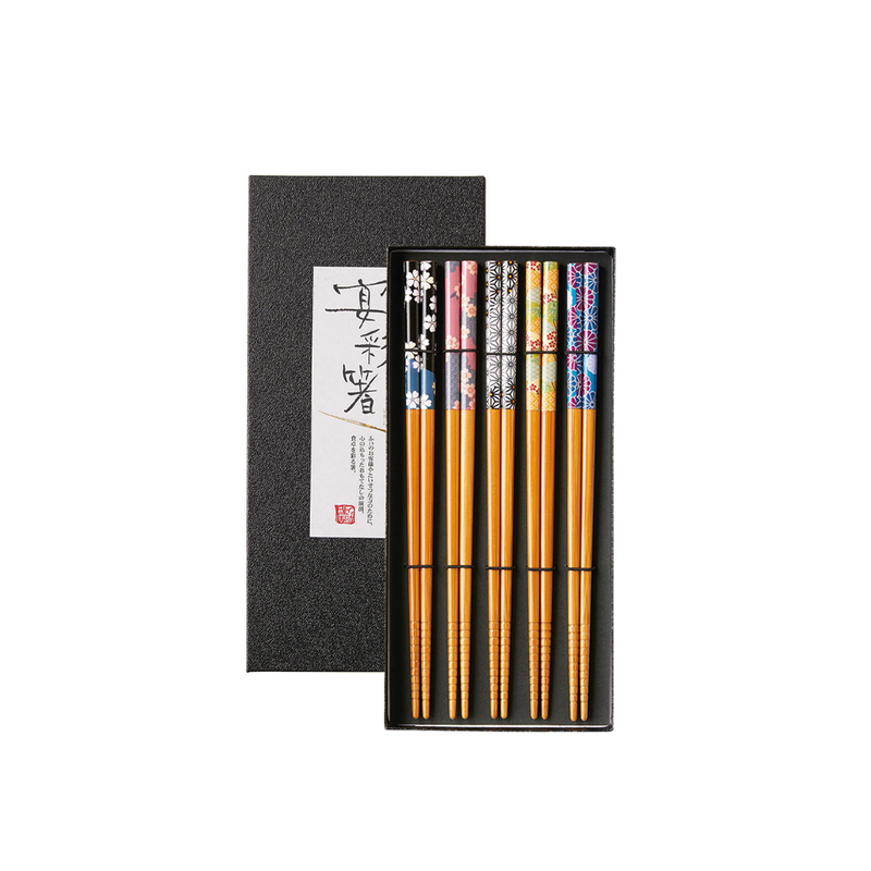 A studio photo of the Ishida Four Seasons Natural Wood Chopsticks set, showing five pairs of elaborately patterned chopsticks in a sleek black gift box with a white textured label.