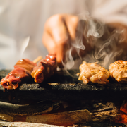 Chicken skewers being grilled over glowing binchotan charcoal, with smoke rising from the hot grill.