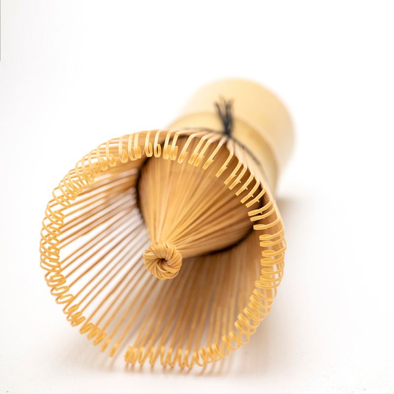 A detailed close-up of a 100-prong bamboo matcha whisk, showing the fine, curved tips for frothing matcha tea.