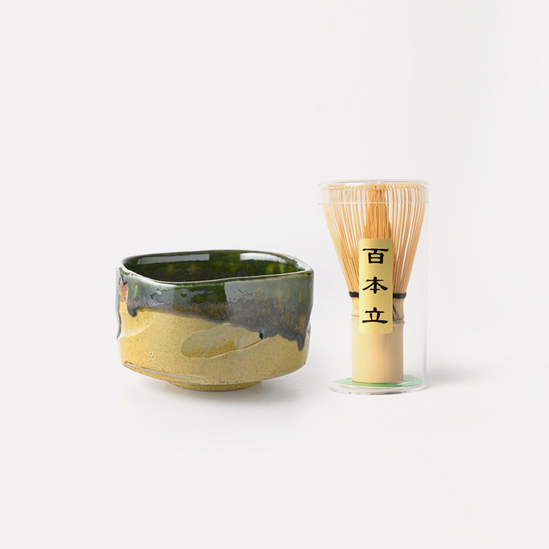A handcrafted Japanese matcha bowl with an Oribe glaze, paired with a traditional 100-prong bamboo Chasen whisk in a transparent protective case.
