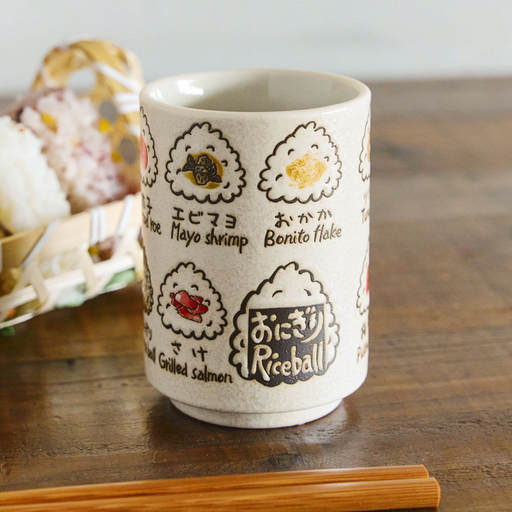 A cylindrical Japanese teacup (yunomi) featuring cute illustrations of various onigiri rice balls, such as Mayo Shrimp, Bonito Flake, and Grilled Salmon, labeled in English and Japanese.