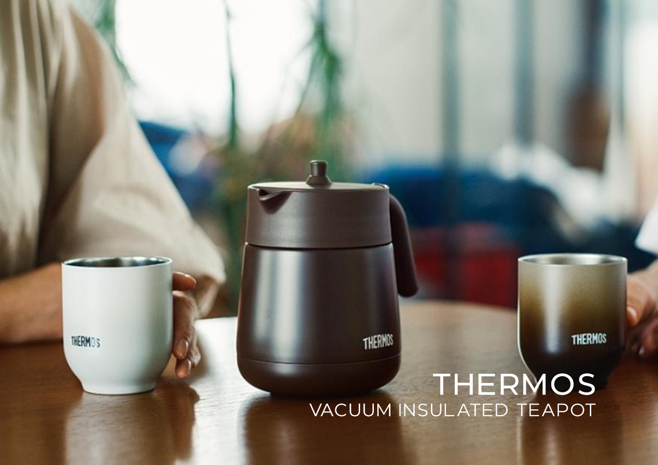 Thermos vacuum insulated teapot with two mugs on a table, blurred background