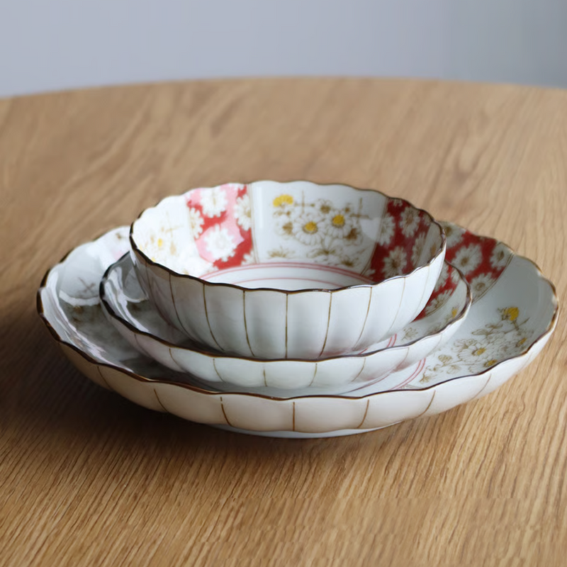 Three Japonica Kikka chrysanthemum-shaped plates stacked on a wooden table, showing the nested sizes and red and white rim details.