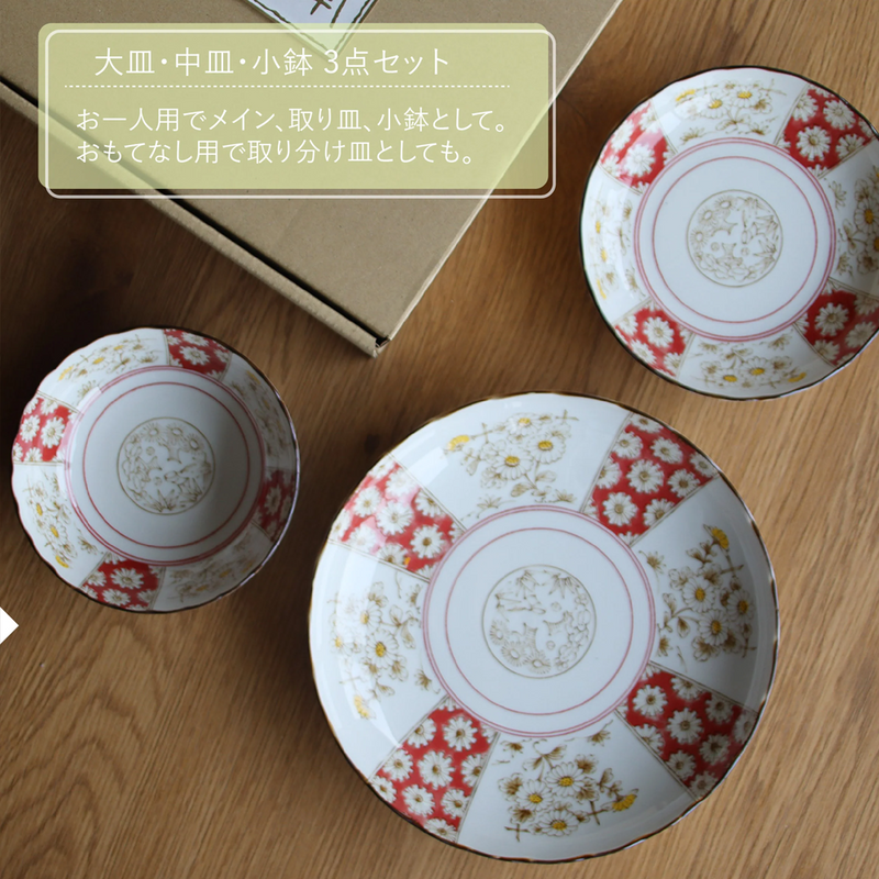 An overhead view of the 3-piece Japonica Kikka set laid out on a wooden table next to a gift box, showing the large plate, medium plate, and small bowl.