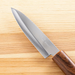 Kai Kitchen fruit knife beside its wooden sheath on a textured grey stone background.