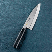 The Kai Seki Magoroku Premium Deba Knife (180mm) laid on a textured blue surface, showcasing its thick, single-bevel blade and traditional hexagonal composite wood handle.
