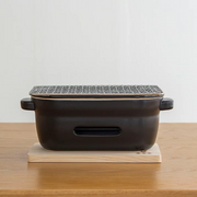 A straight side-on view of the Kamoshika Douguten konro grill, showing the ventilation slot and handles, sitting on its wooden base.