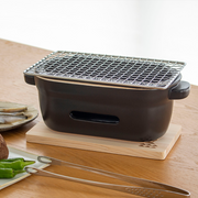 The Kamoshika Douguten konro grill on its wooden base, positioned on a light wood table next to tongs and a plate of food.

