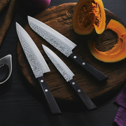 Three Kaneyoshi Hammered VG10 Japanese knives from the series displayed on a wooden cutting board with a freshly cut pumpkin.


