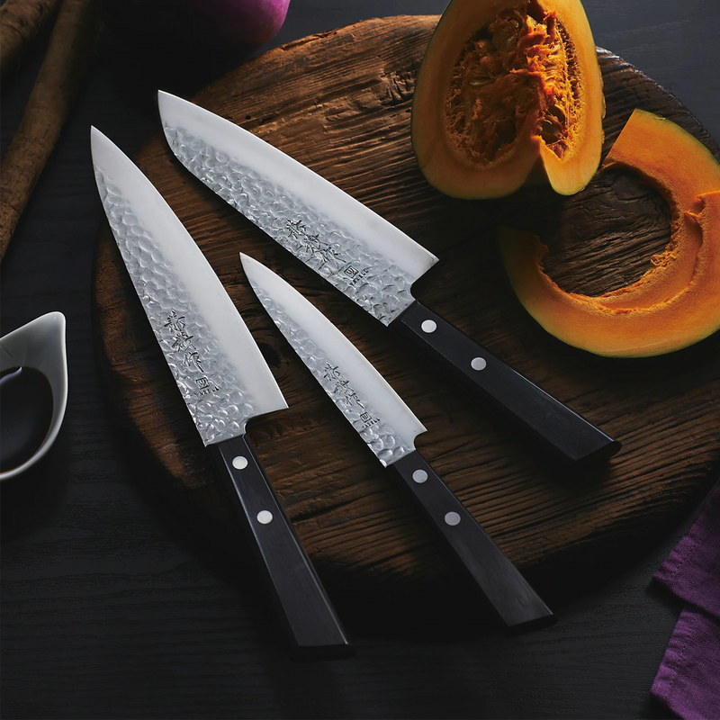 Three Kaneyoshi Hammered VG10 Japanese knives from the series displayed on a wooden cutting board with a freshly cut pumpkin.

