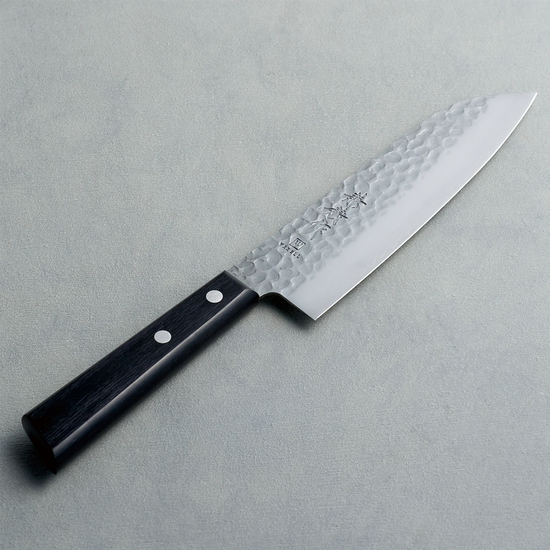 The Kaneyoshi Hammered VG10 Japanese Santoku Knife (165mm) on a grey textured background, showing its tsuchime (hammered) finish and black reinforced wood handle.

