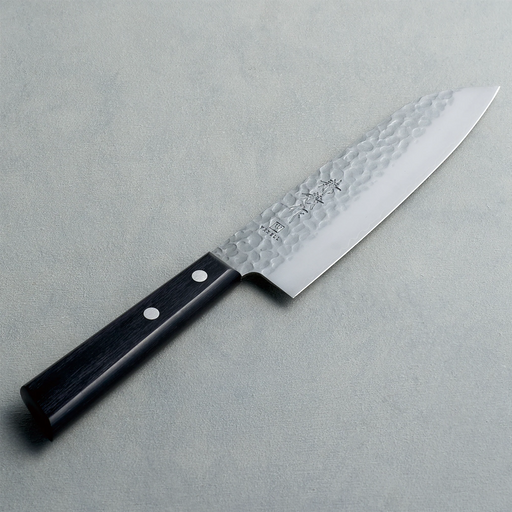 The Kaneyoshi Hammered VG10 Japanese Santoku Knife (165mm) on a grey textured background, showing its tsuchime (hammered) finish and black reinforced wood handle.

