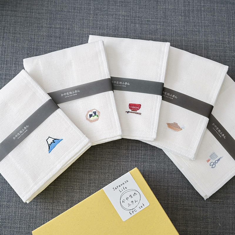 The Kayanuno Embroidered Cloth Gift Set, showing the five different white cloths with their unique embroidery (Mt. Fuji, sushi, donabe, etc.) fanned out next to their yellow gift box.
