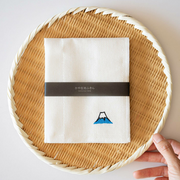 The white Kayanuno kitchen cloth, neatly folded to display its delicate Mt. Fuji embroidery, resting in a Japanese bamboo basket.
