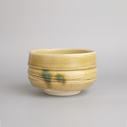 A side view of the Kiseto Yellow Seto Japanese matcha bowl, highlighting its classic shape, horizontal grooves, and the green glaze detail on its crackled yellow surface.