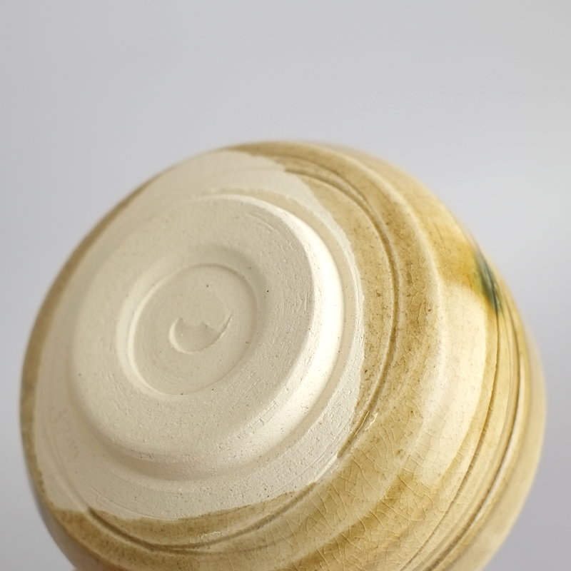 A close-up view of the base of the Kiseto matcha bowl, showing the unglazed foot and the texture of the yellow crackle glaze with throwing lines.