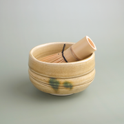 A traditional Japanese matcha tea set, including a Kiseto (Yellow Seto) ceramic bowl with a yellow crackle glaze and a 100-prong bamboo whisk (chasen).
