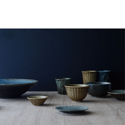 A collection of Japanese ceramic bowls and cups in varying earthy tones, displayed against a dark backdrop, showcasing traditional pottery craftsmanship.