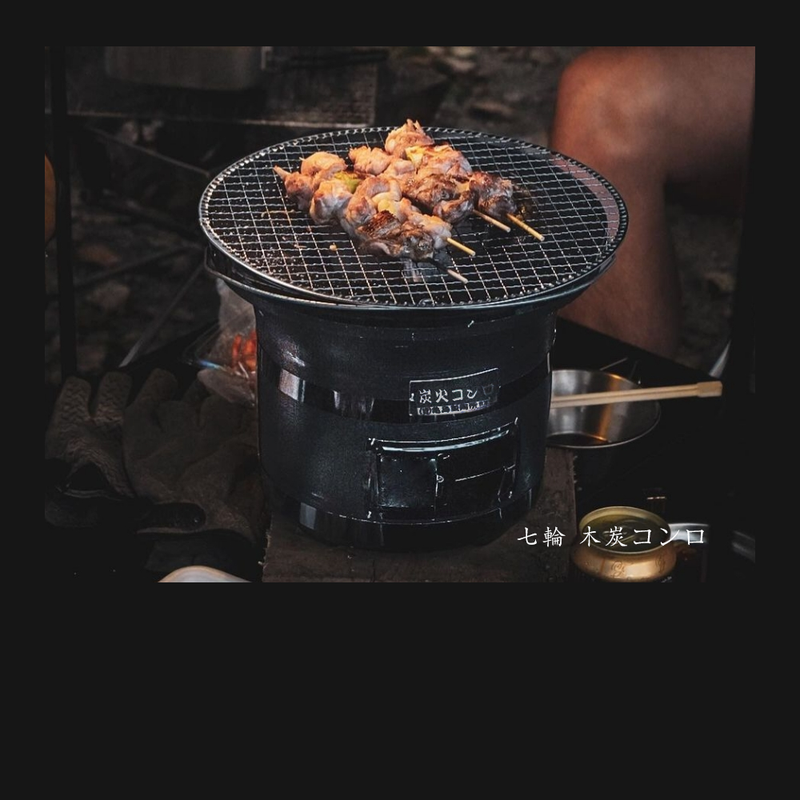 Mikawa Portable Konro Grill in use, grilling skewers on a round mesh grate outdoors.