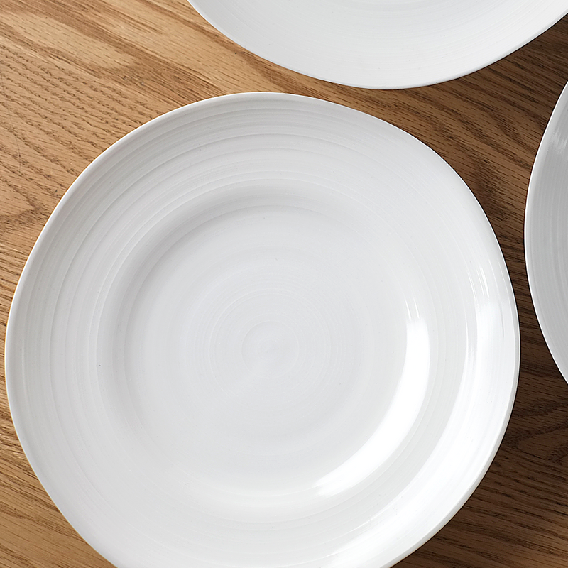 A top-down view of the white Kushime dinner plate, showing its subtle concentric lines, placed on a dark wood surface.