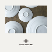 The underside of several white Kushime plates, showing the foot and concentric texture, with the Oda Pottery logo in the corner.

