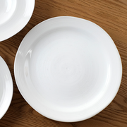 A top-down view of the white porcelain Kushime Dinner Plate on a dark wood surface.
