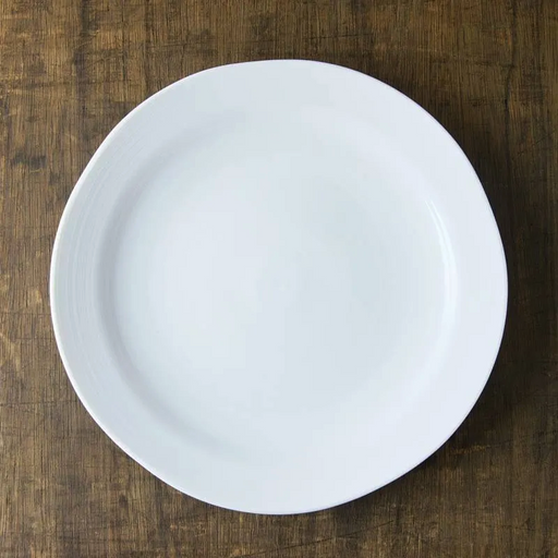A top-down view of the white porcelain Kushime Dinner Plate on a dark wood surface.
