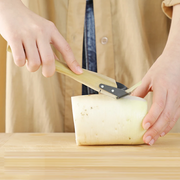 A person using the Kyoto Katsugu forged peeler to peel a large piece of daikon radish, demonstrating its use in a kitchen setting. 