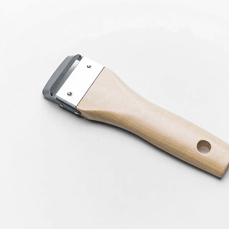 A detailed close-up of the Kyoto Katsugu Forged Peeler, showing the sharp high-carbon steel blade and traditional wooden handle.

