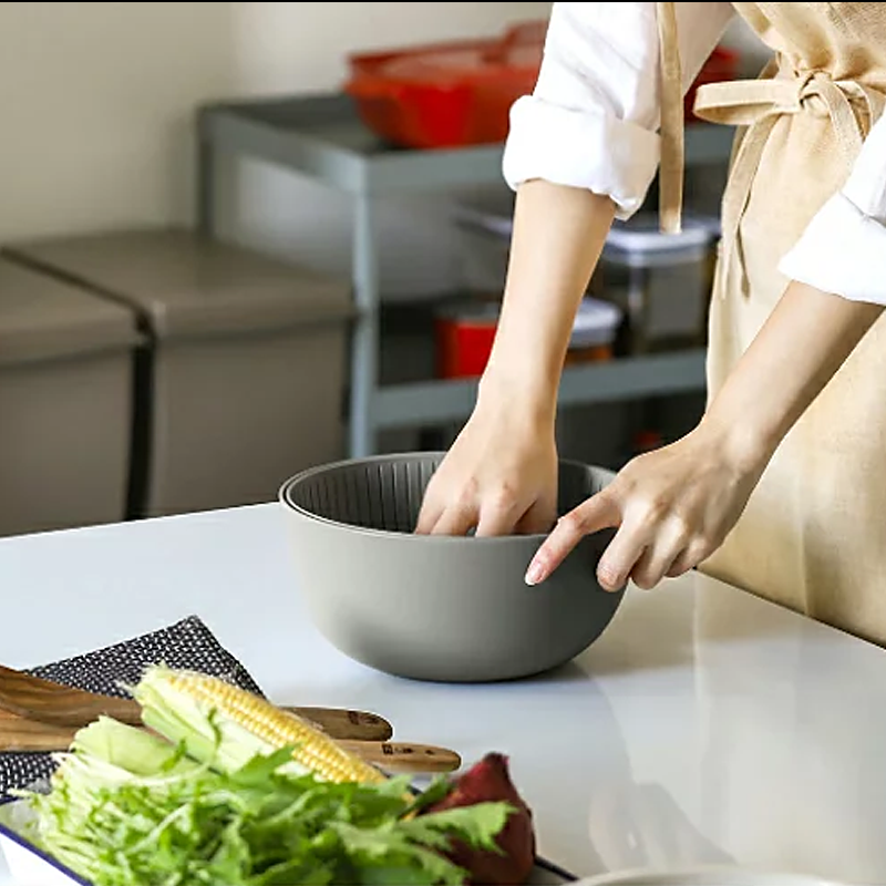 A person in an apron using their hands to mix ingredients inside the large grey Like-it bowl on a kitchen counter.